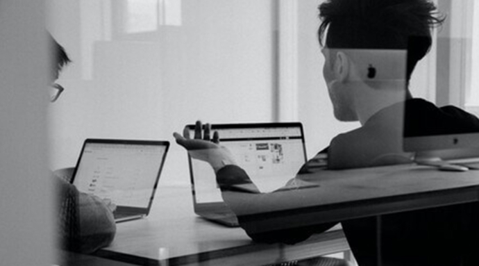 Behind the glass partition view of two colleagues planning with laptops open